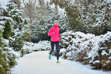 Winter running and fitness in park: happy woman runner jogging in snow, outdoor sport concept
