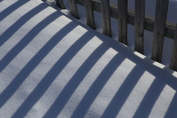 The alternation of light and dark bands. The shadow of the fence in the snow.