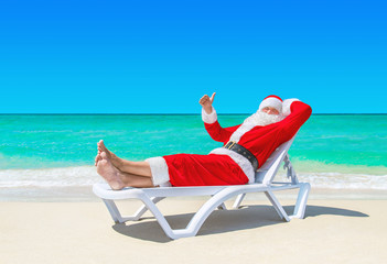 Santa Claus thumbs up gesturing on sunlounger at tropical beach