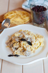 Fettuccine carbonara in a white bowl with bacon and mushrooms.