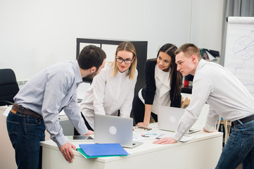 Young business people sitting in office during meeting and discussing with paperwork using laptops