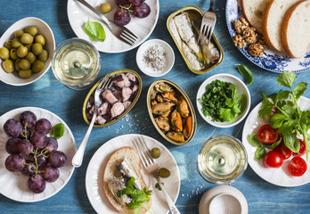 Seafood snacks table - canned sardines, mussels, octopus, grape, olives, tomato and two glasses white wine on wooden table, top view. Flat lay