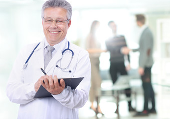 Happy smiling mature doctor writing on clipboard