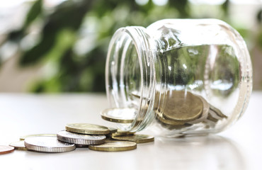 The concept of saving money . The money is scattered from a glass jar on the table.