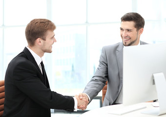 Fototapeta premium Two happy young men shaking hands while sitting at the office