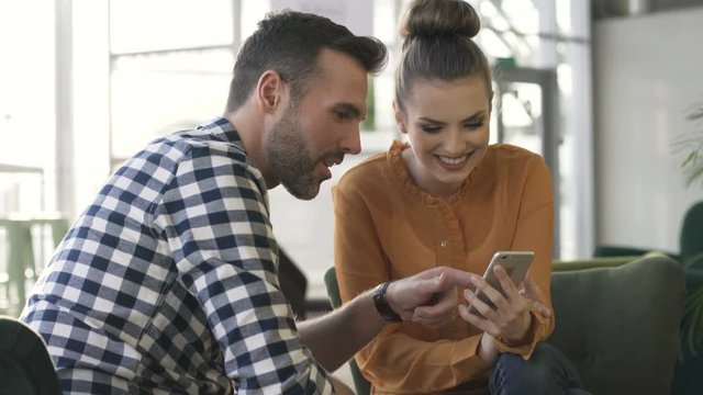 Happy couple having fun at cafe browsing smartphone together
