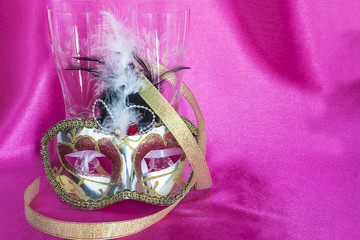 holidays concept/two glasses of champagne, carnival mask and golden ribbon on purple satin background
