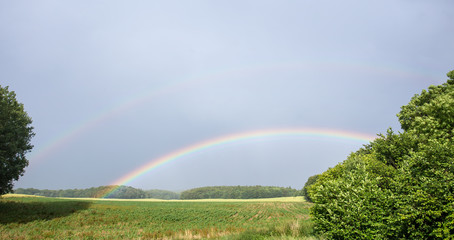 ein doppelter Regenbogen steht über einem Feld