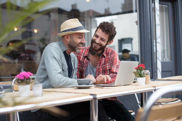 Gay couple sat sharing laptop outside cafe