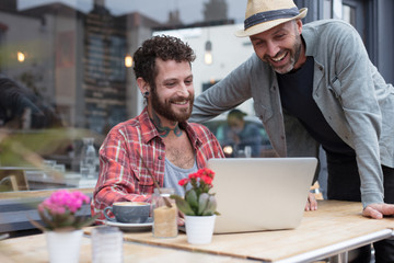Gay couple sat sharing laptop outside cafe