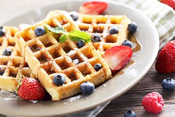 Homemade waffles with berries in plate on grey wooden table