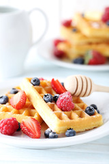 Homemade waffles with berries in plate on blue wooden table