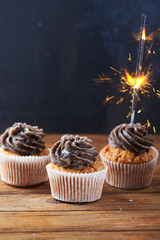 Close view at tasty chocolate cup cakes with sparkler light at wooden background. Vertical shot. Copy space.