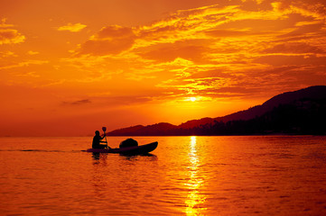 Naklejka na ściany i meble Man on a boat in the sea at beautiful sunset