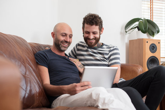 Gay Couple Sat Cuddling On Sofa, Sharing Tablet