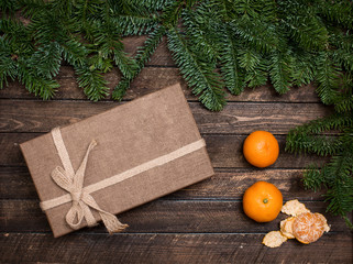 Gift box and tangerines with fir branches on rustic wooden backgound