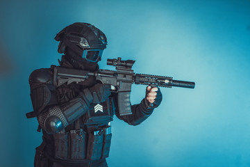 Member of the SWAT squad with an assault rifle in a black uniform on blue background. Special...