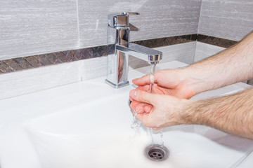 A man washes his hands in the bathroom.