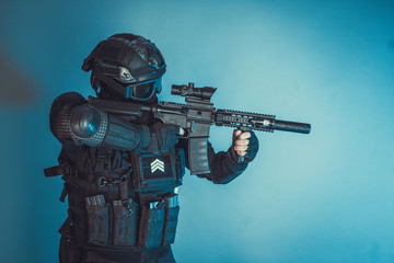 Member of the SWAT squad with an assault rifle in a black uniform on blue background. Special...