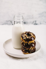Fresh baked gluten free chocolate donuts and bottle of milk on white table