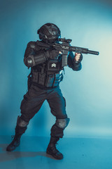 Member of the SWAT squad with an assault rifle in a black uniform on blue background. Special weapons and tactics. Special Forces.