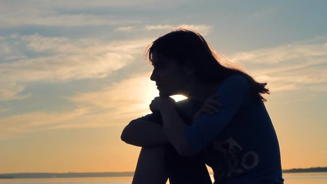 Silhouette profile of young woman sitting against sunset sky