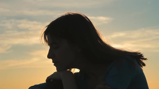 Silhouette profile of woman sitting against sunset sky