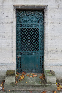 Bat door - turquoise closed steel entrance gate of an old tomb / crypt at a graveyard. Ornaments of grapes, faces and in the round iron arch the nocturnal flying animal, spreading its wings.