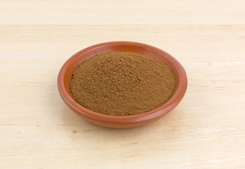 Carob powder in a bowl on a wood table.