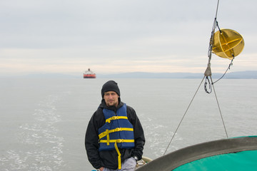 A man in a blue life jacket  is staying on sailboay near gold radar reflector