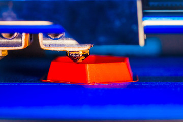 3d printer printing red faceted geometric shapes on a blue background close-up. Bright contrast...