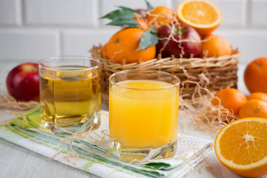 Fresh orange and apple juice in a glass on a background of fruit baskets