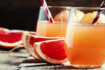 Grapefruit juice and fresh citrus fruits, dark vintage wooden ba