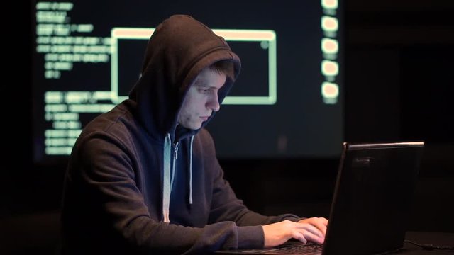 The Hacker in a Hood with Notebook Cracks a Computer Code