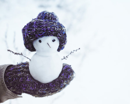 Small snowman in a knitted cap on a mitten against the background of snow in the winter.  Festive background with a lovely snowman. Christmas Card copyspace