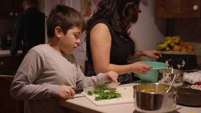 A young boy chopping vegetables in the kitchen with his mother