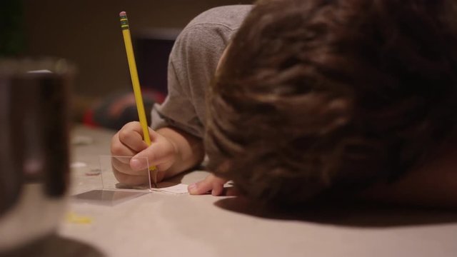 A boy sitting at the kitchen counter, writing and putting a christmas sticker on a piece of paper