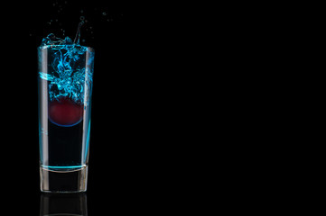 Blue cocktail with cherry, splash in glass isolated on black background. Shot alcohol drink.