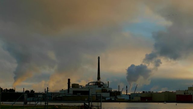 Fast moving factory smokestacks time lapse at dawn. Plumes of smoke or steam rising, flocks of birds flying through as daybreak comes.