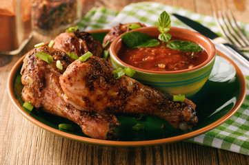 Roasted chicken legs and tomato sauce on wooden background.