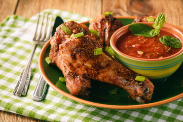 Roasted chicken legs and tomato sauce on wooden background.