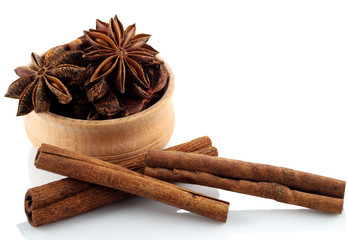 Star anise in a wooden bowl with cinnamon sticks on a white back
