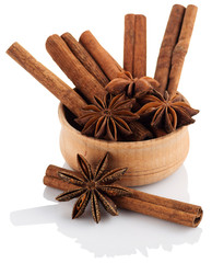 Star anise in a wooden bowl with cinnamon sticks on a white back