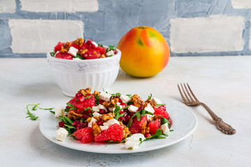 Vegetarian salad with grapefruit, arugula, feta cheese, pomegranate seeds and walnuts, caramelized in honey. White plate on light table.