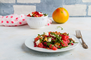 Vegetarian salad with grapefruit, arugula, feta cheese, pomegranate seeds and walnuts, caramelized in honey. White plate on light table.