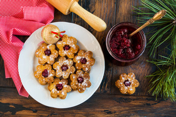 Christmas Linzer homemade cookies with strawberry jam on wooden background. White plate, festive decoration, top view.