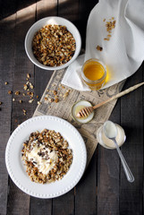 Homemade oatmeal granola with peanuts, yogurt and honey on white plates on dark table, sunny morning