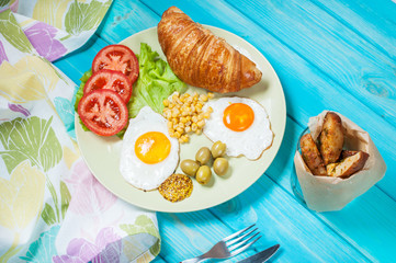 Breakfast on a wooden table. Fried eggs, tomato, croissant