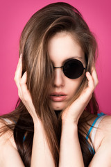 Beautiful fashionable woman in black sunglasses. Pink background. Girl in sunglasses. Round glasses.