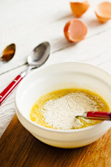 Mixing ingredients for paleo pancakes in white bowl - eggs, mashed banana, coconut flour on white rustic wooden background.  Close up